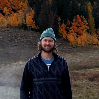 David DeBonis, founder of seeking synthesis, standing in a forest in front of autumn leaves.